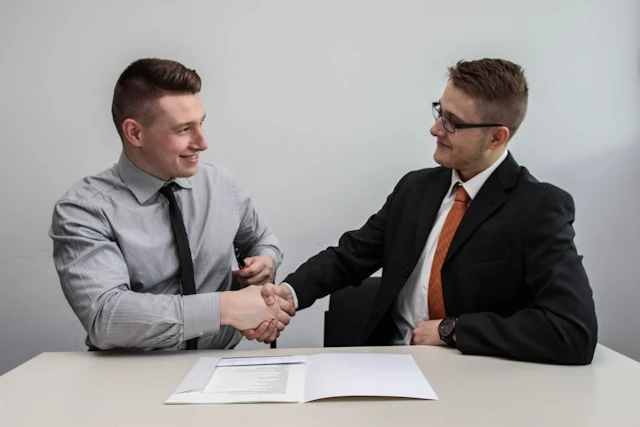 Two men in suits shaking hands over a document